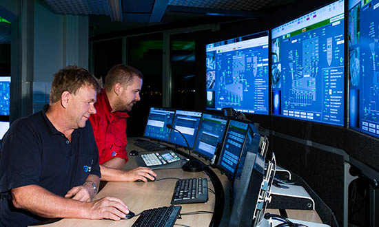 Two people looking at a wall of screens with keyboard and mouse